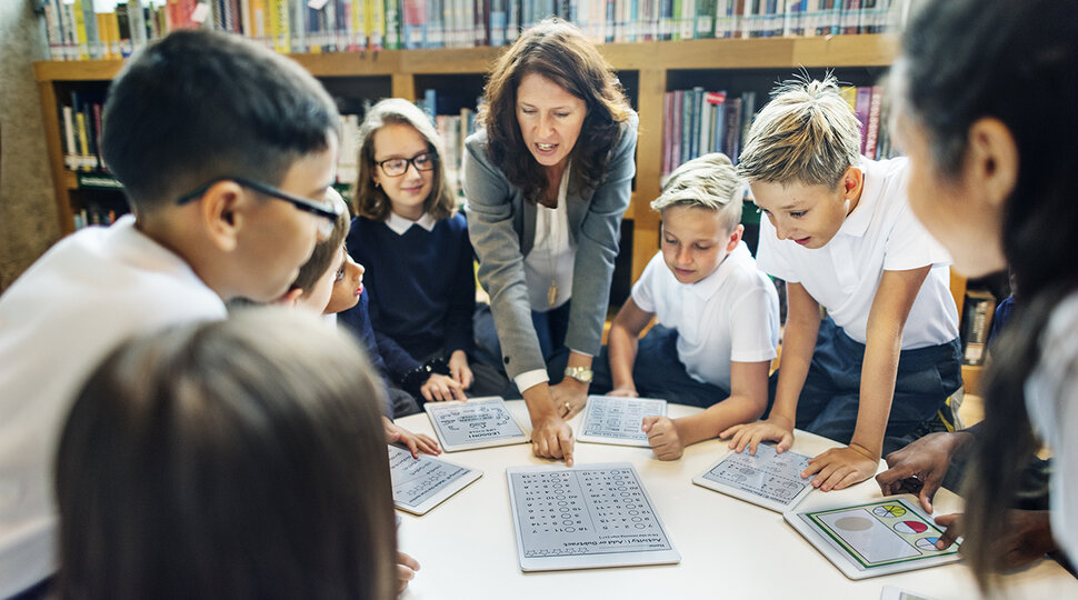 Eine Erwachsene und mehrere Kinder beugen sich über einen Tisch und schauen sich Fragebögen an