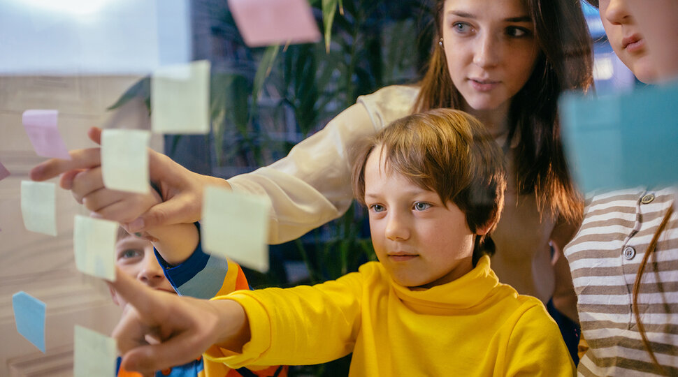 Kinder und Jugendliche zeigen auf bunte Post-its, die am Fenster hängen