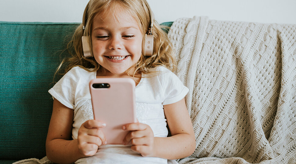 Ein Mädchen mit Kopfhörern schaut auf ein Smartphone und freut sich