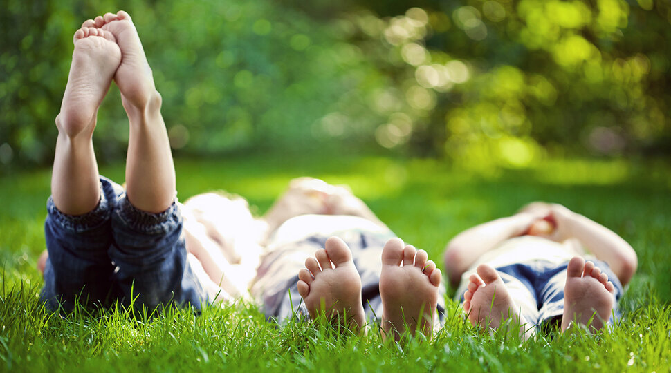 drei Kinder liegen auf einer Wiese und schauen in den Himmel