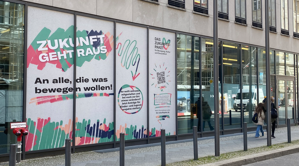 Ein Bild von der Fensterfassade des BMFSFJ in Berlin, auf die Werbung für das Zukunftspaket geklebt wurde.