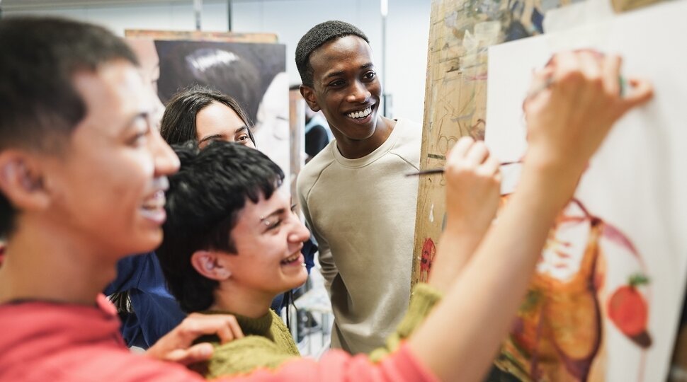 Junge Menschen stehen vor einer Wand mit Zeichnungen und lachen