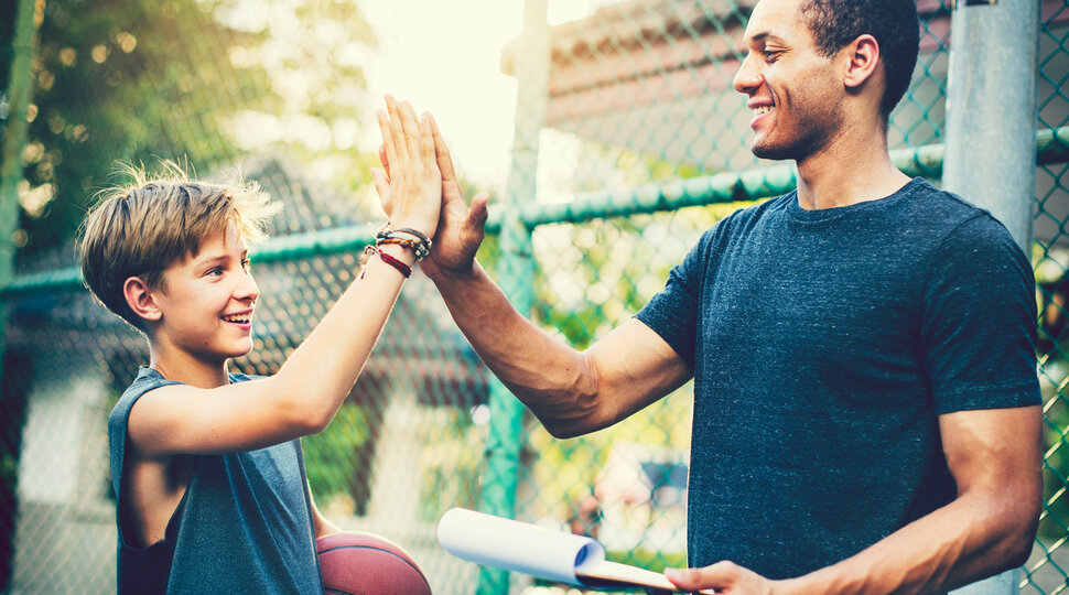 Ein Junge hat einen Basketball in der Hand und klatscht mit seinem Coach ab