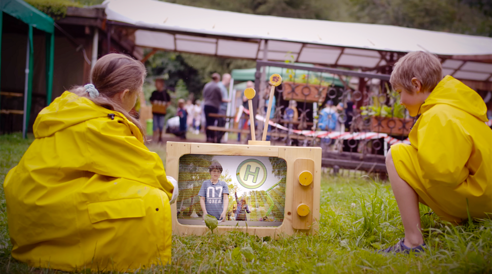 Zwei Kinder in gelben Regenmänteln vor einem Fernseher aus Holz