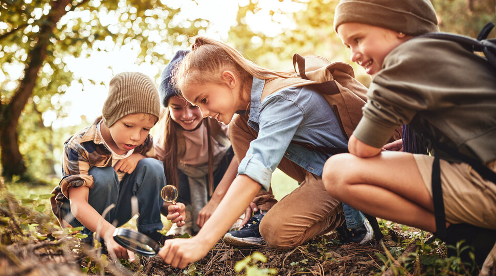 Kinder und Jugendliche mit einer Lupe draußen in der Natur