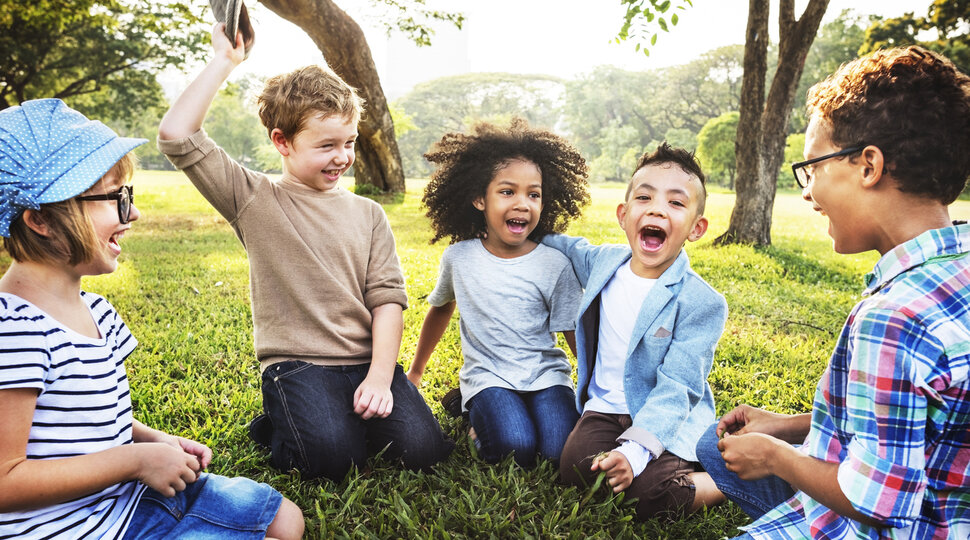 Fünf Kinder sitzen auf einer Wiese und lachen