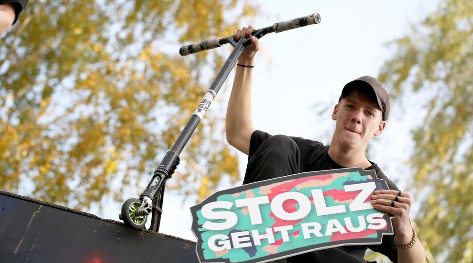 Ein Jugendlicher sitzt auf einer Skaterampe und hält ein Schild it der Aufschrift "Stolz geht raus"