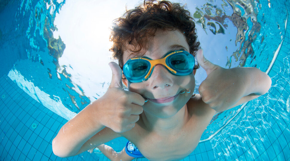 Ein Junge unter Wasser mit einer Taucherbrille hält beide Daumen hoch