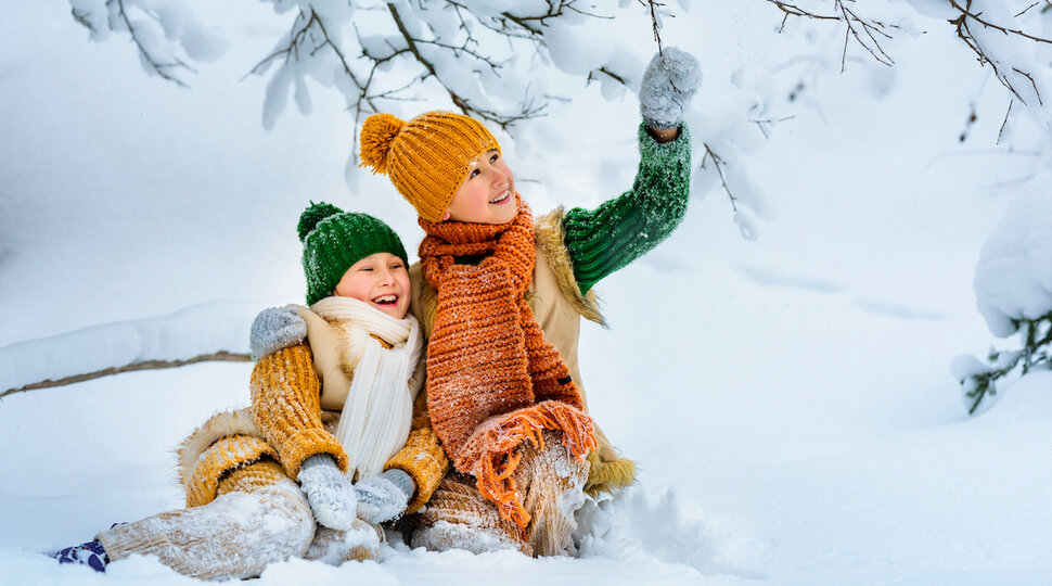 Zwei Kinder sitzen im Schnee, lachen und winken