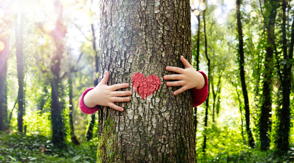 Ein Kind umarmt einen Baum, an den ein rotes Herz gemalt ist