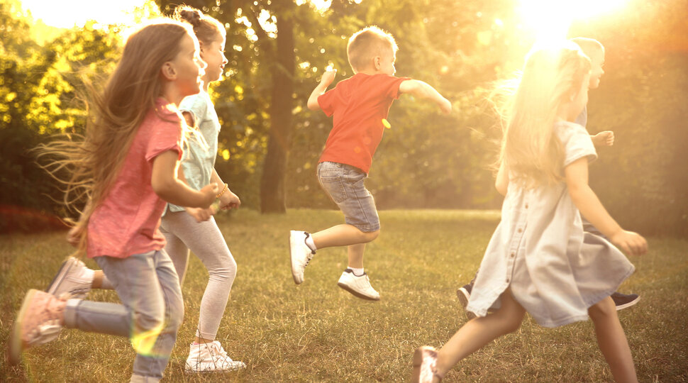 Fünf Kinder rennen durch einen Park, der Sonne entgegen