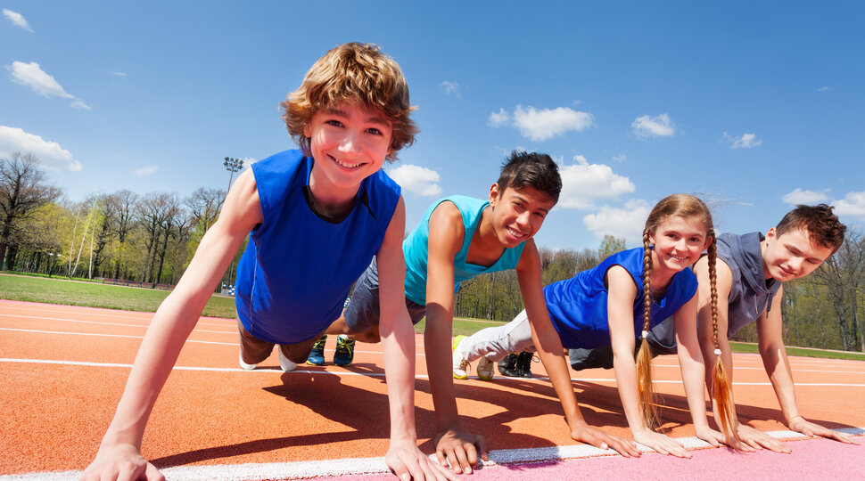 Vier Kinder in Sportkleidung, die sich mit den Händen auf einer Sprintstrecke abstützen