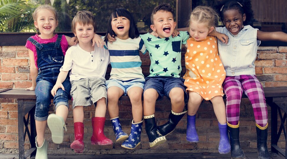 Verschiedene Kinder sitzen fröhlich auf einer Bank