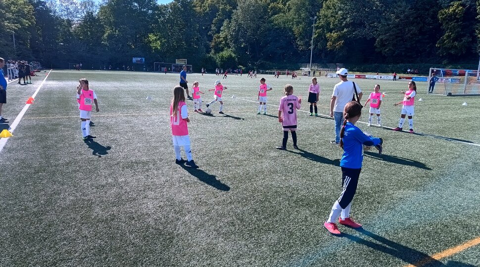 mädchen fußballmannschaft in rosa Trikots und weißen Hosen beim Training, vorne im Bild Torfrau in blauem Trikot mit schwarzer Hose