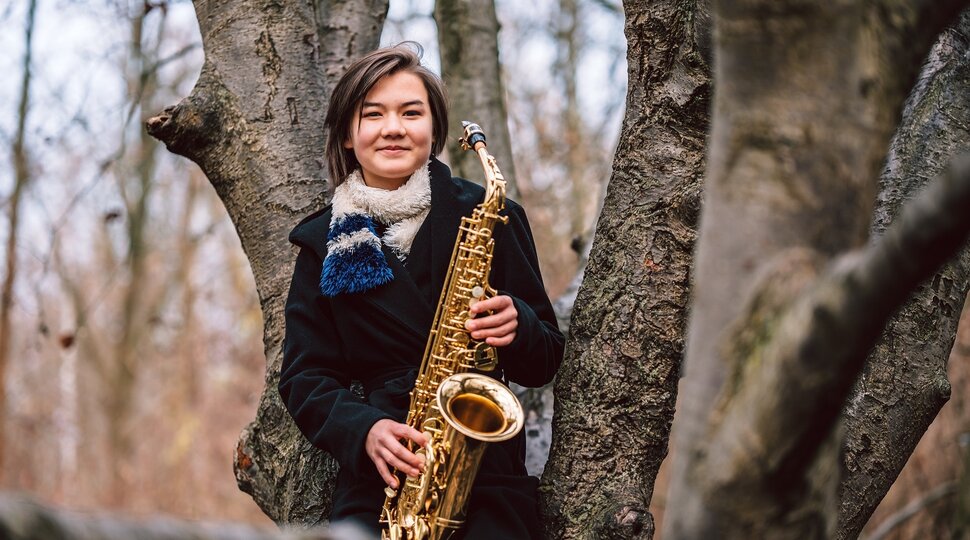 Mädchen mit einem Saxophon sitzt im Baum