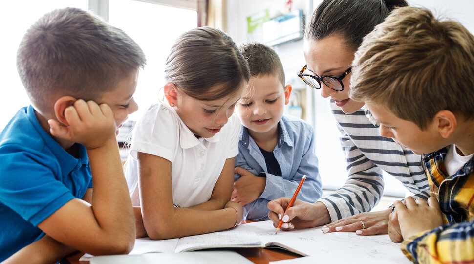 Eine pädagogische Fachkraft mit vier Kindern an einem Tisch