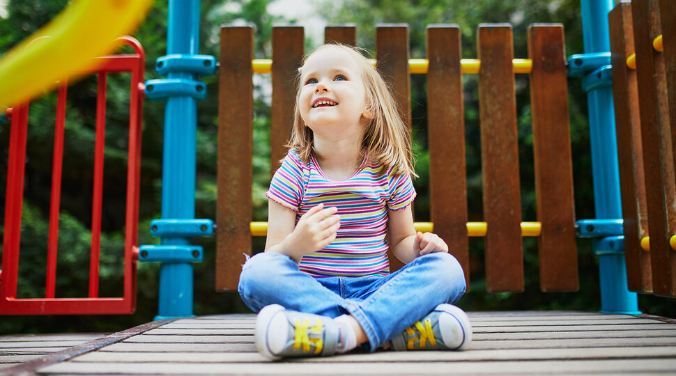 Ein Mädchen sitzt auf einem Spielplatz und schaut in den Himmel