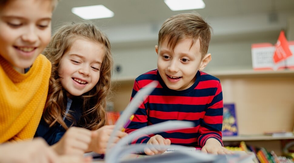 Drei Kinder blättern in einer Broschüre und lachen