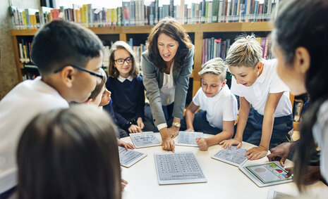 Eine Erwachsene und mehrere Kinder beugen sich über einen Tisch und schauen sich Fragebögen an