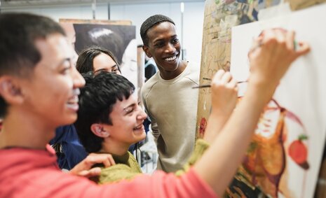 Junge Menschen stehen vor einer Wand mit Zeichnungen und lachen