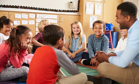 Grundschulkinder und Lehrer sitzen auf dem Fußboden in einem Kreis