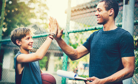 Ein Junge hat einen Basketball in der Hand und klatscht mit seinem Coach ab