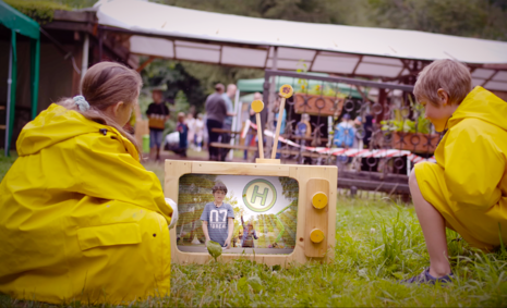 Zwei Kinder in gelben Regenmänteln vor einem Fernseher aus Holz