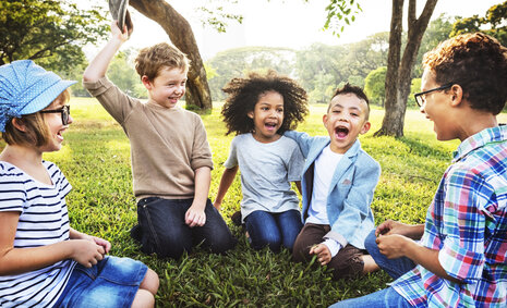 Fünf Kinder sitzen auf einer Wiese und lachen