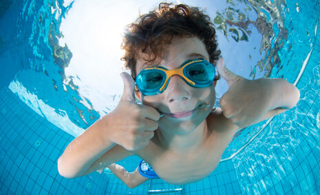Ein Junge unter Wasser mit einer Taucherbrille hält beide Daumen hoch