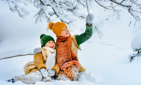 Zwei Kinder sitzen im Schnee, lachen und winken