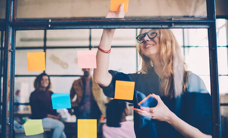 Eine Jugendliche hängt verschiedenfarbige Post-its an ein Fenster