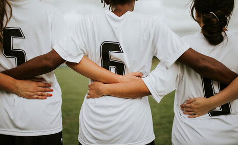 Drei Fußballerinnen mit verschiedenen kulturellen Hintergründen verschränken ihre Arme