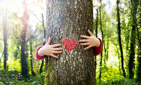 Ein Kind umarmt einen Baum, an den ein rotes Herz gemalt ist