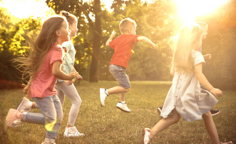 Fünf Kinder rennen durch einen Park, der Sonne entgegen