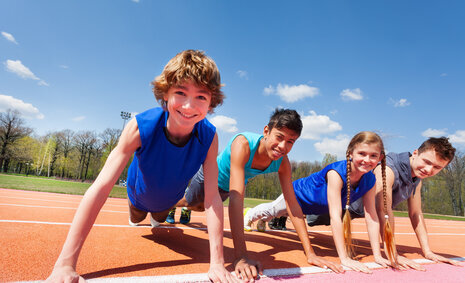 Vier Kinder in Sportkleidung, die sich mit den Händen auf einer Sprintstrecke abstützen