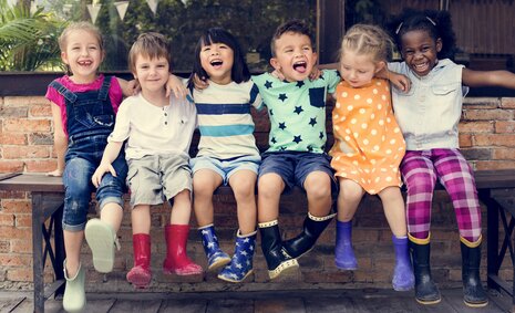 Verschiedene Kinder sitzen fröhlich auf einer Bank