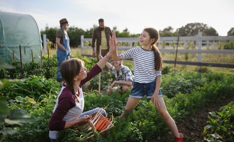 Ein Mädchen und eine Erwachsene klatschen in einem Gemeinschaftsgarten ab