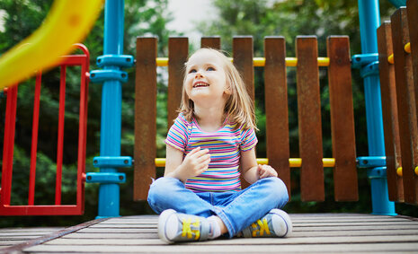 Ein Mädchen sitzt auf einem Spielplatz und schaut in den Himmel