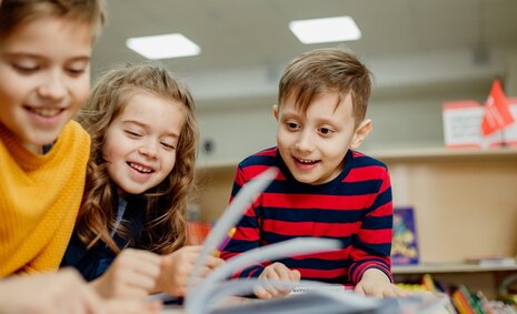 Drei Kinder blättern in einer Broschüre und lachen