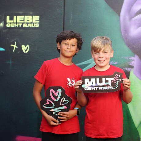 Zwei Jungen halten Pappschilder mit der Aufschrift MUT geht raus und einem Herz-Symbol