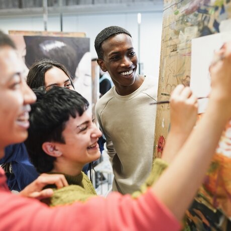 Junge Menschen stehen vor einer Wand mit Zeichnungen und lachen