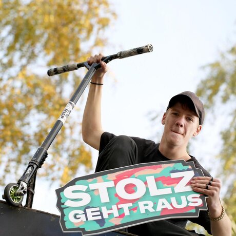 Ein Jugendlicher sitzt auf einer Skaterampe und hält ein Schild it der Aufschrift "Stolz geht raus"