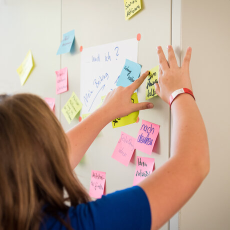 Eine Person klebt einen Post-it an eine Wand mit vielen Post-its