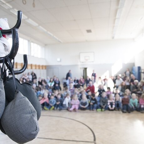 Eine Gruppe von Kindern sitzt in einer Turnhalle und schaut auf eine Bühne